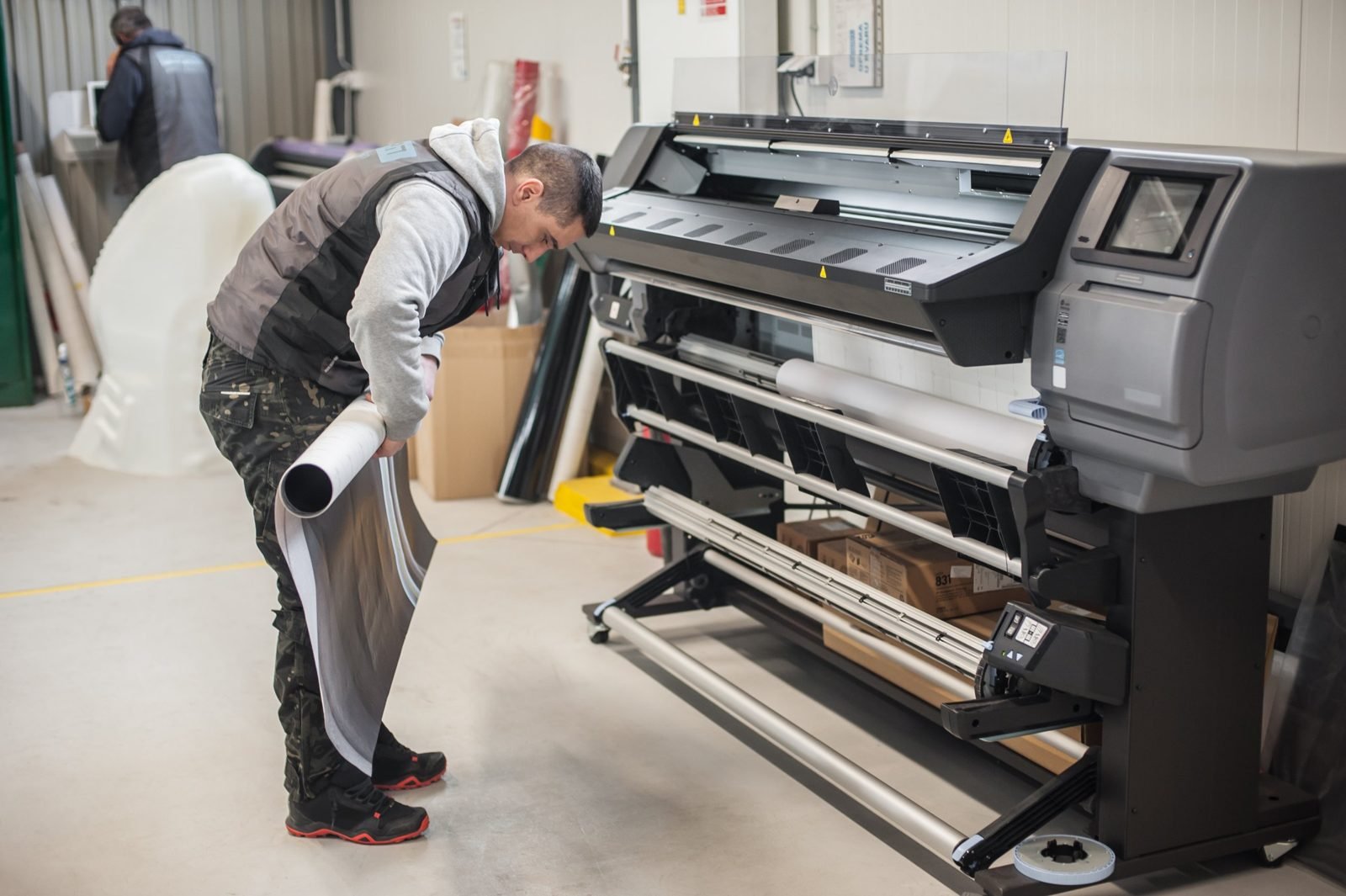 Un opérateur contrôle un rouleau imprimé devant une imprimante grand format